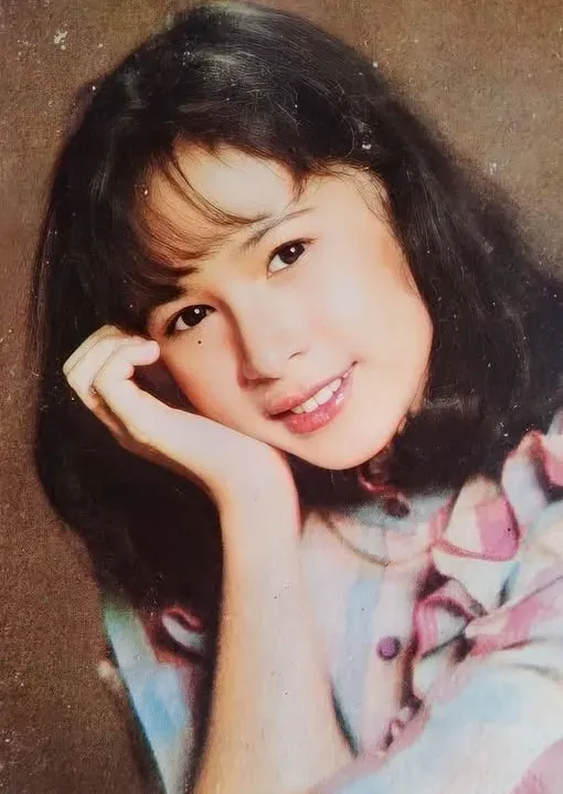 Vintage portrait of a young girl with curly hair resting her chin on her hand, softly lit against a dark background.