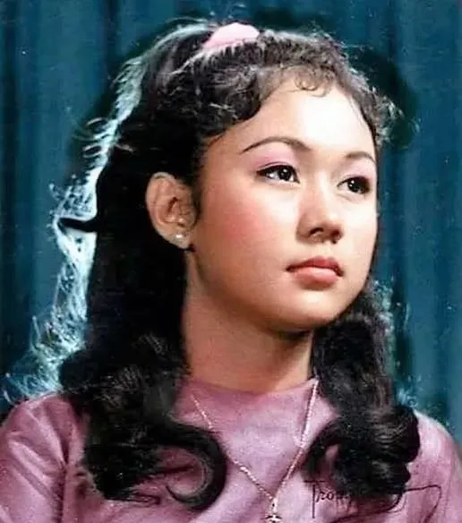 Vintage portrait of a young girl with long dark hair wearing a pink top, looking to the side against a dark background.