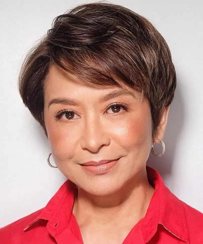 Studio portrait of a woman with short brown hair in a red top, smiling against a grey background.