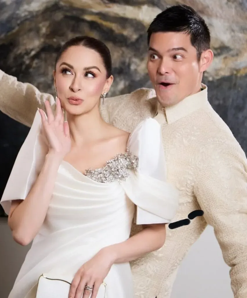 Photo of a couple in formal white attire, the woman in a beaded gown and the man in a white suit, posed playfully together.