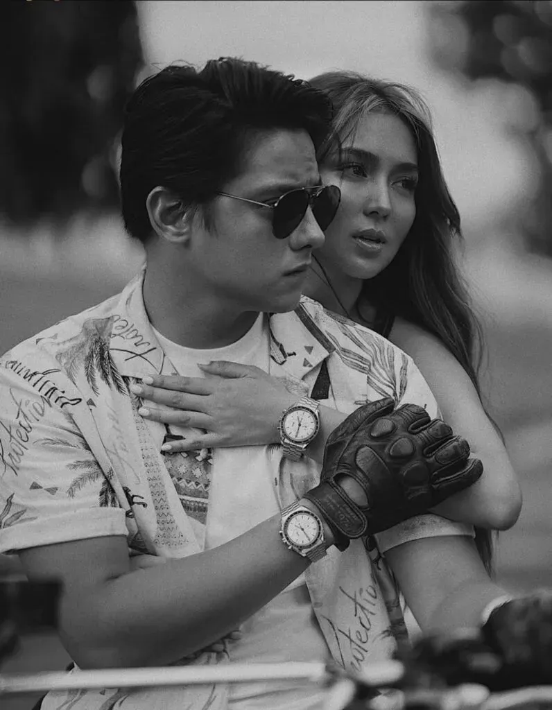 Black-and-white photo of a couple in sunglasses posed closely together, hands clasped.