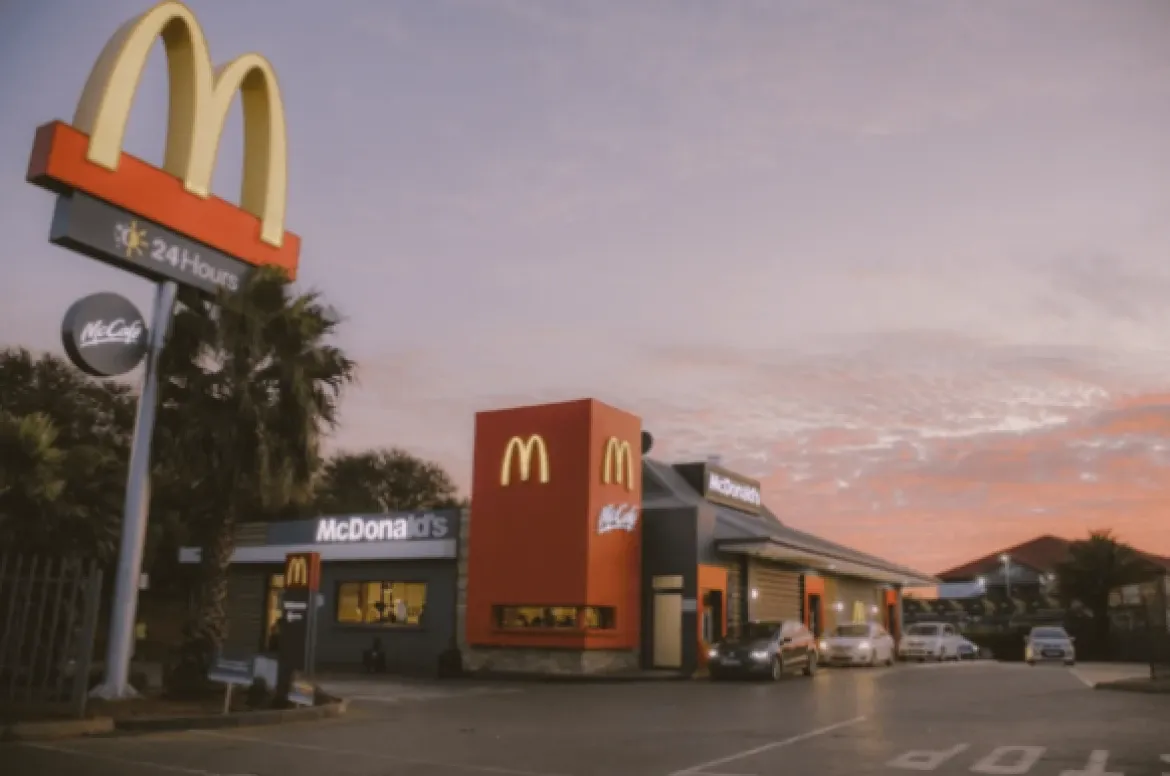 Photo of a McDonald’s restaurant with its golden-arches sign and palm trees at dusk.