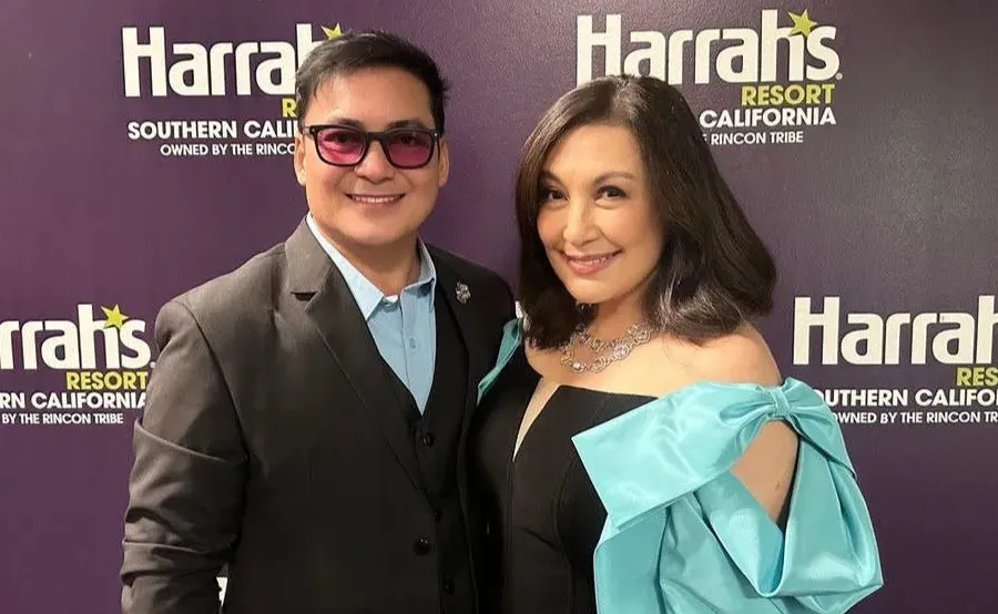 Photo of a man in glasses and a woman in a teal dress posed together in front of a “Harrah’s” backdrop.