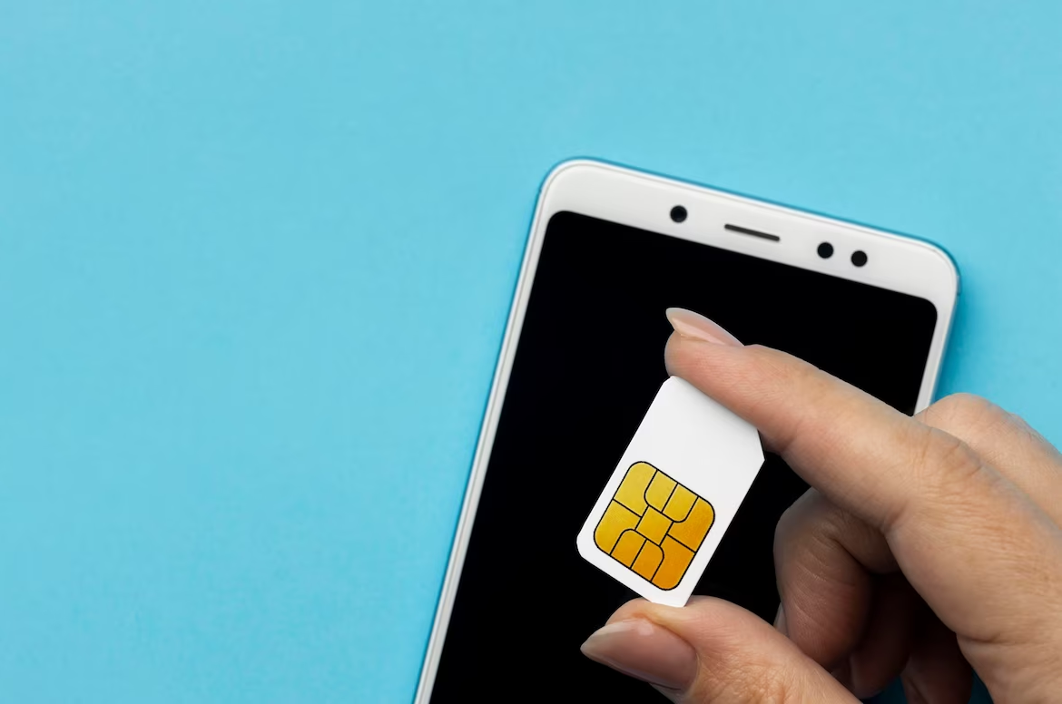 Photo of a hand inserting a SIM card into the tray of a smartphone against a blue background.
