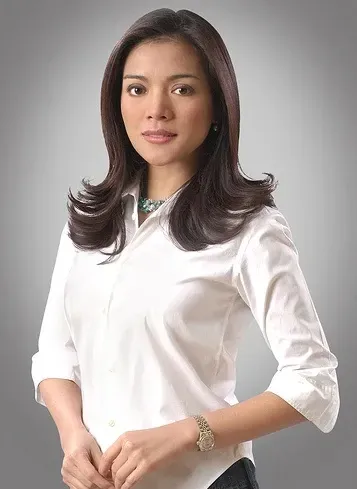 Studio portrait of a woman with long dark hair in a white blouse, against a light background.