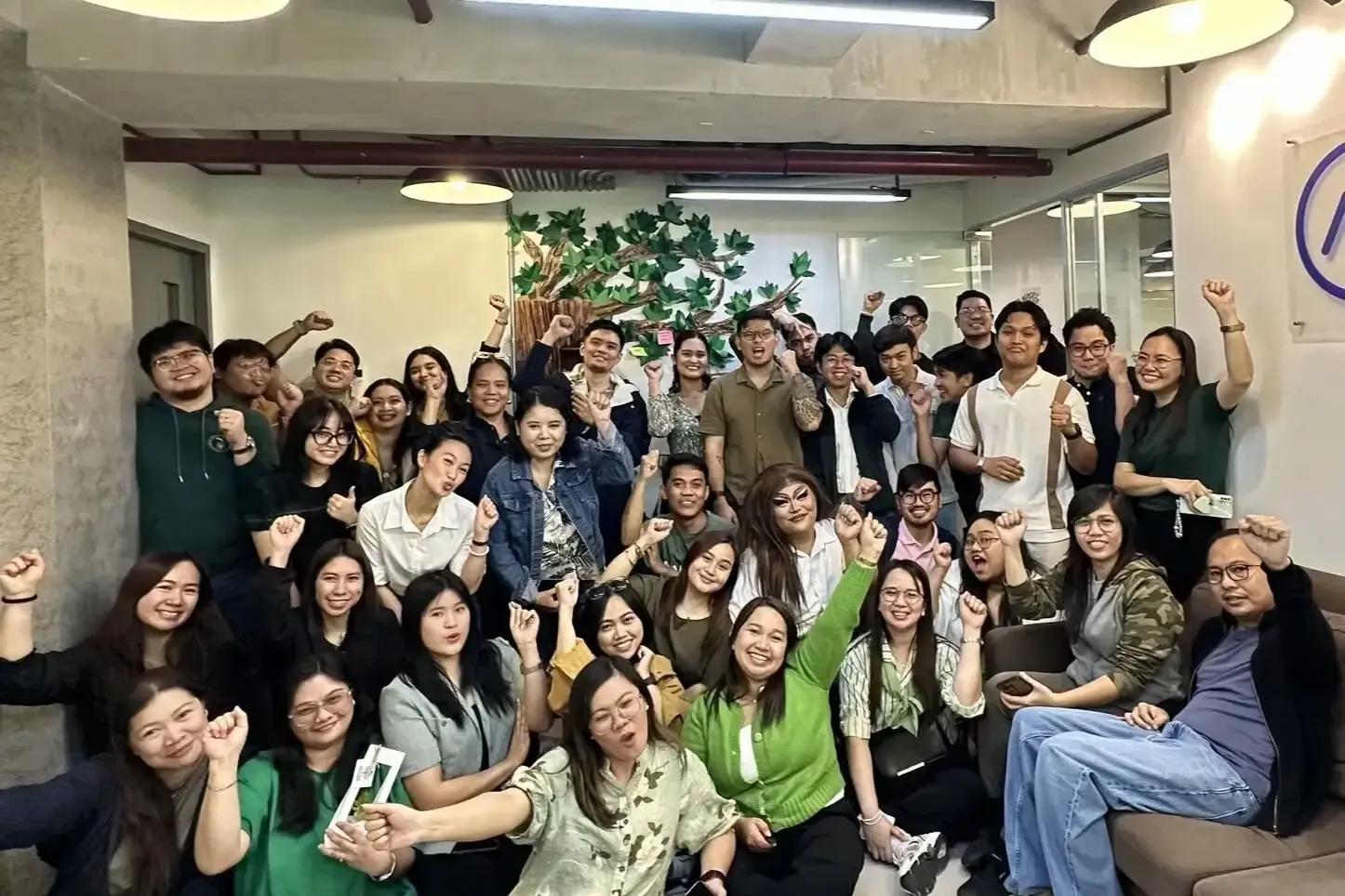 Group photo of a large team posed together smiling in an office, many wearing green.