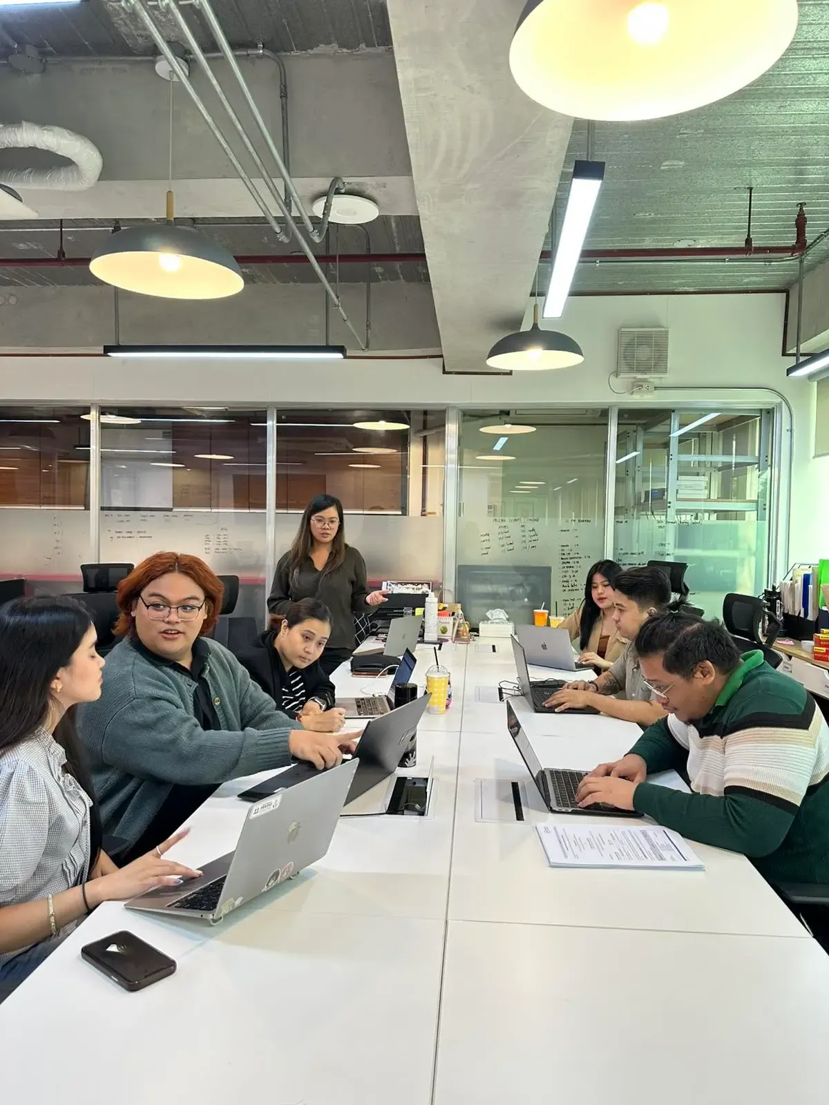 Photo of a team of professionals seated around tables in a modern open-plan office, one person standing and gesturing.