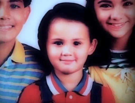 Group photo of three smiling people posed closely together, two adults and a child, in casual attire.