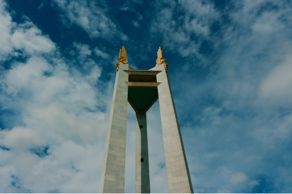 Photo looking up at a tall monument obelisk against a blue sky with scattered clouds.