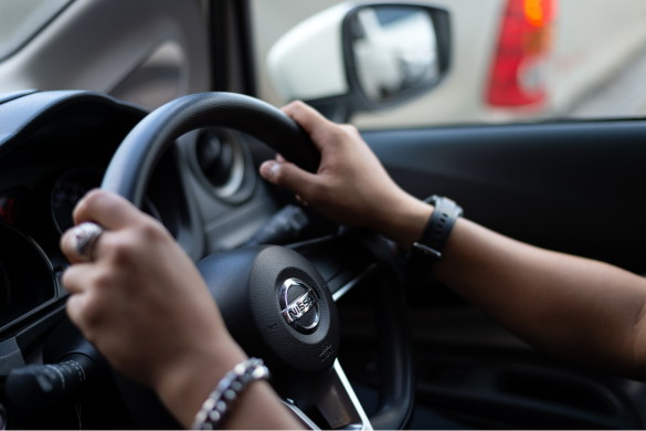 Close-up photo of hands gripping a car steering wheel while driving.