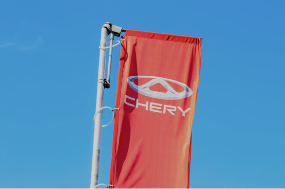 Photo of a red flag bearing the “CHERY” automotive logo against a blue sky.