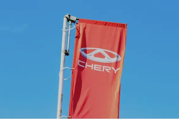 Photo of a red flag bearing the “CHERY” automotive logo against a blue sky.