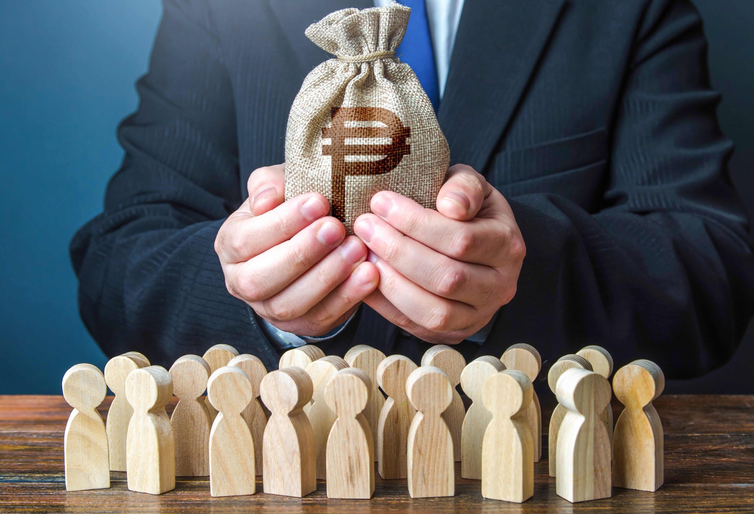 Photo of a person in a suit cupping a small money bag above rows of wooden peg figures, symbolizing fund allocation.