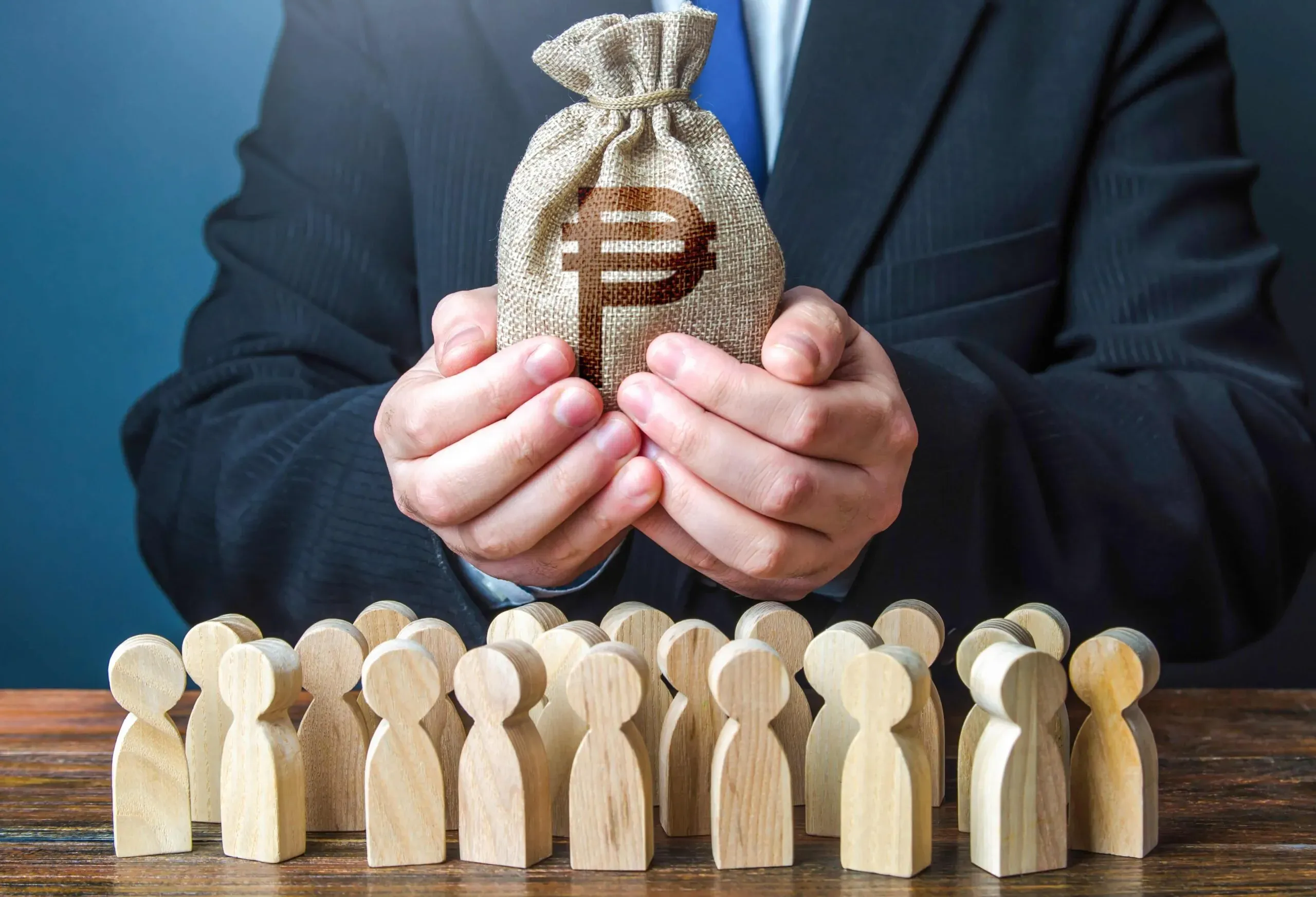 Photo of a person in a suit cupping a small money bag above rows of wooden peg figures, symbolizing fund allocation.