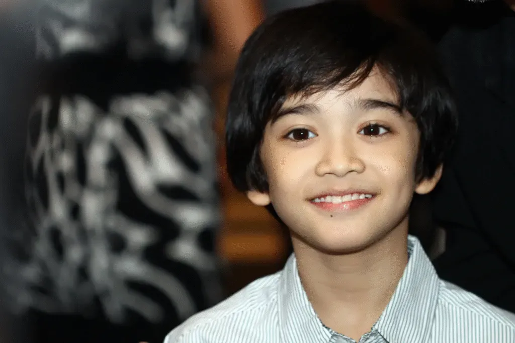 Black-and-white portrait of a smiling young boy with tousled dark hair wearing a collared shirt.